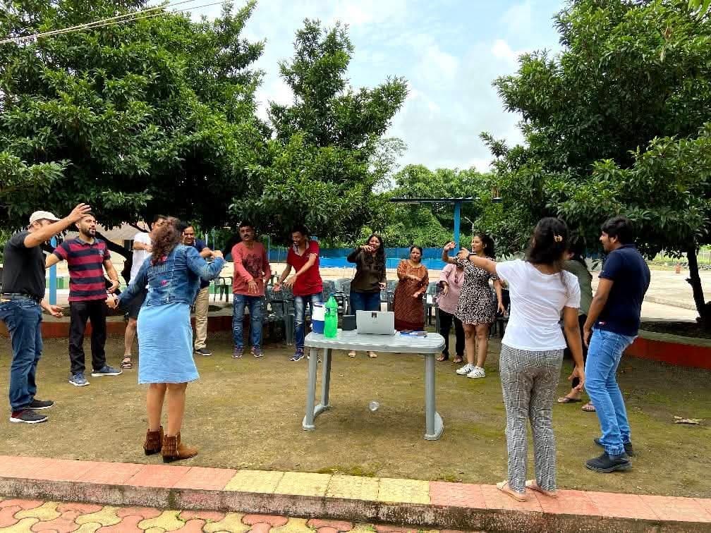 A group standing in a circle outdoors among trees, following a hand exercise together