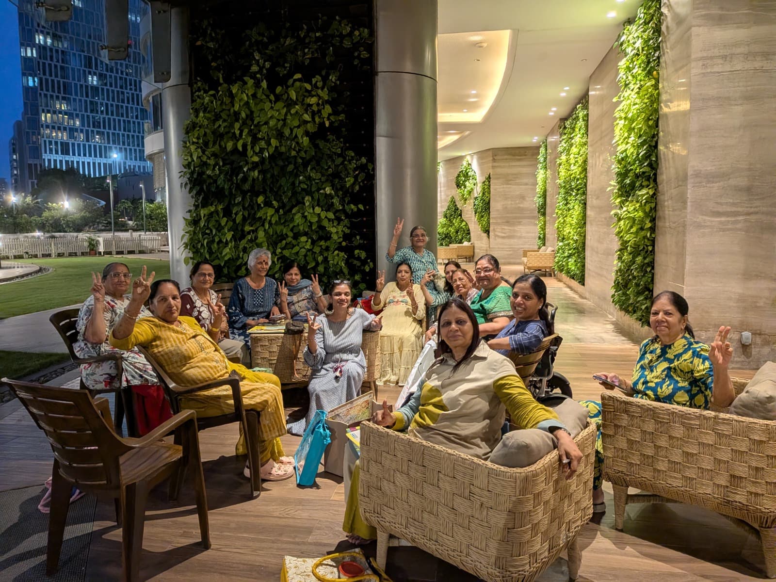 Women seated together in a circle of chairs in a building lobby at dusk, smiling and waving